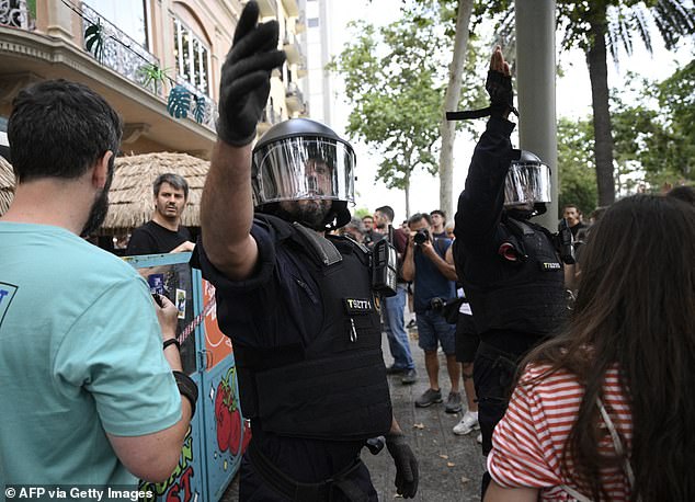 Anti-riot forces gesture as demonstrators put symbolic cordon on a bar-restaurant window during a protest against mass tourism on Barcelona's Las Ramblas alley, on July 6, 2024