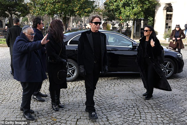 Lloyd cut a solemn figure today as he led mourners through the cemetery wearing black velvet jacket, black trousers and shirt paired with black gloves and his signature sunglasses