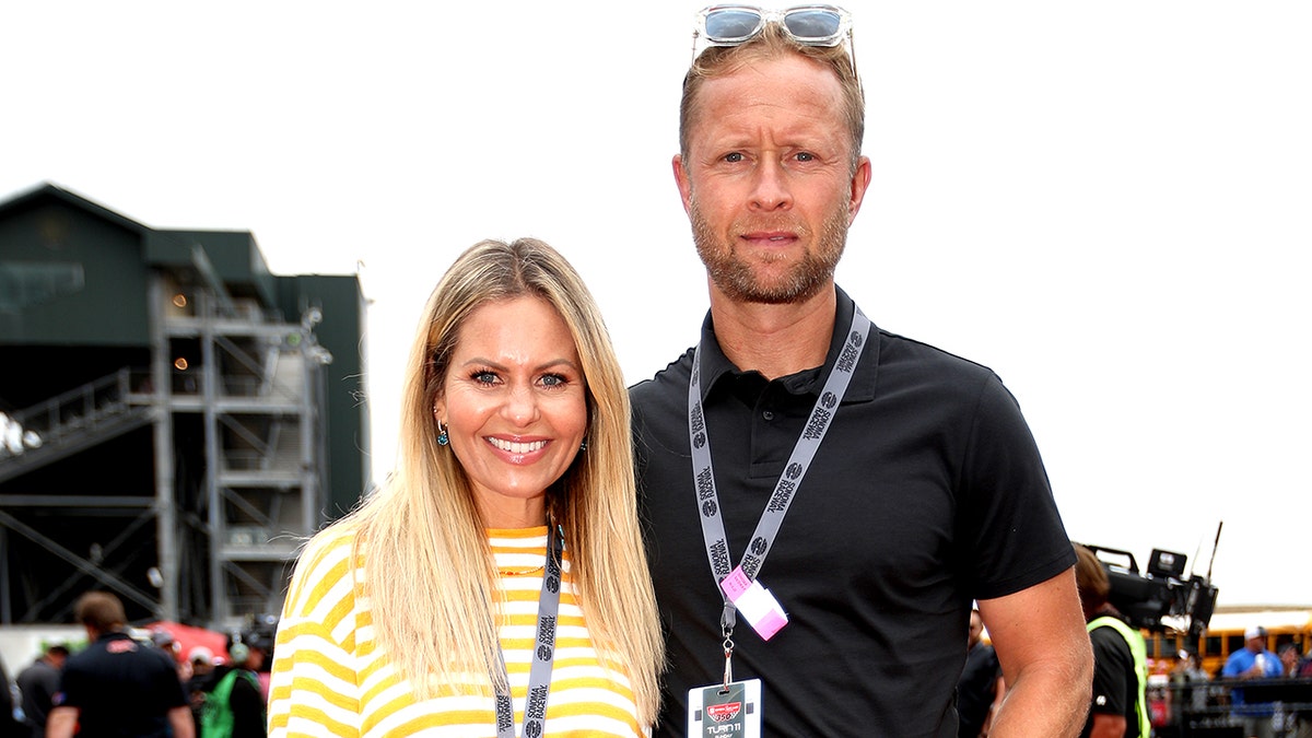 Candace Cameron Bure in a yellow striped shirt smiles big with husband Val