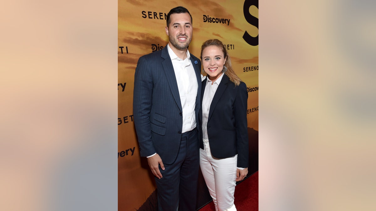 Jinger Duggar Vuolo in a blazer and a white outfit posing with her husband.