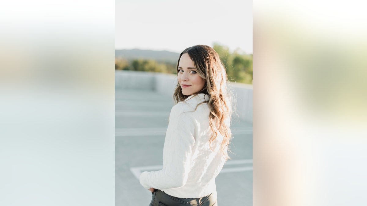 Jinger Duggar wearing a white shirt with her back turned and smiling at the camera.