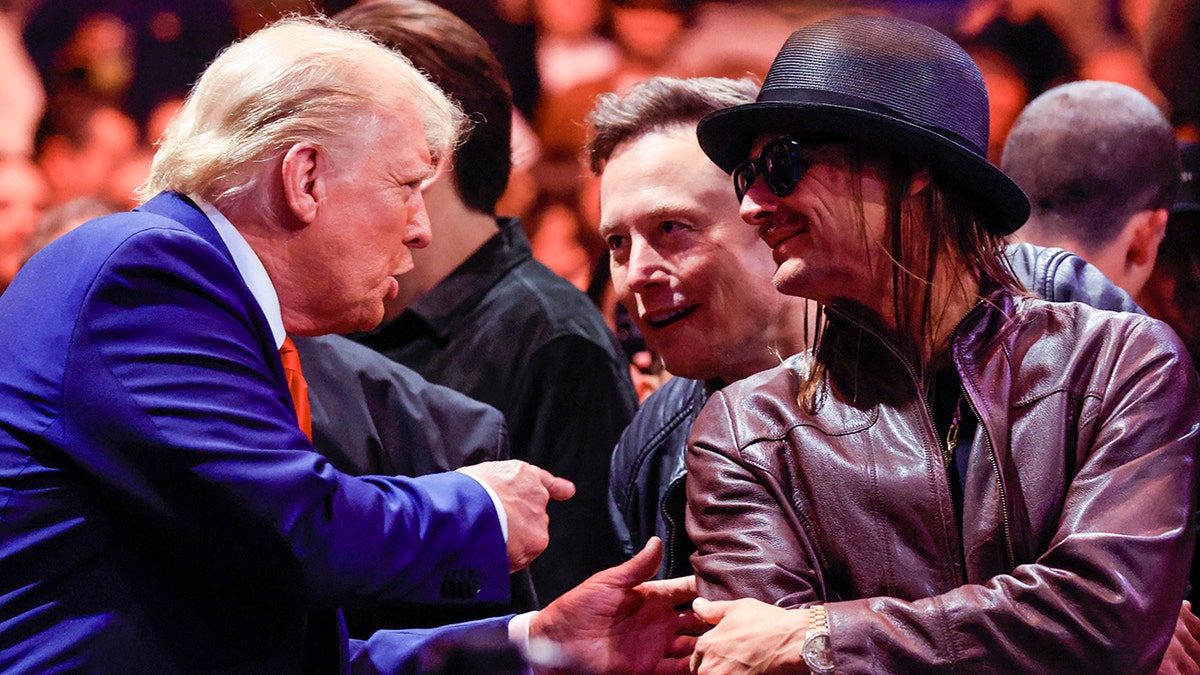 President Trump in a blue suit and red tie points at Elon Musk in a leather jacket and Kid Rock in a leather jacket and hat at the UFC fight in NYC