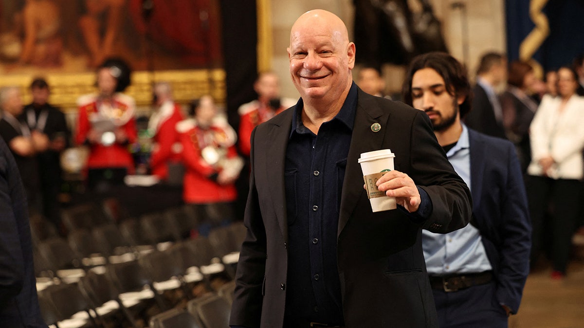 Comedian Jeff Ross smiles in a black suit holding a cup of coffee walking into the Rotunda of the U.S. Capitol ahead of the inauguration