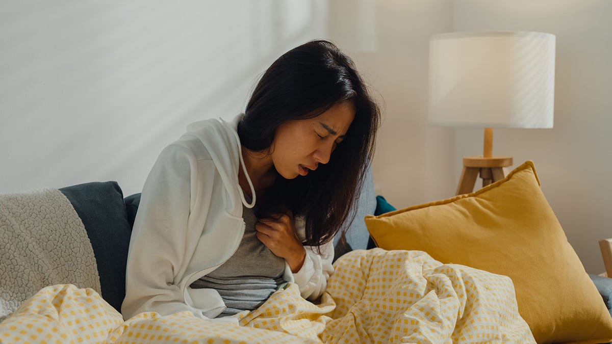 sick woman sitting on sofa holding her chest