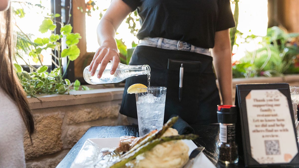 waitress pours a bottle of sparkling water into a glass