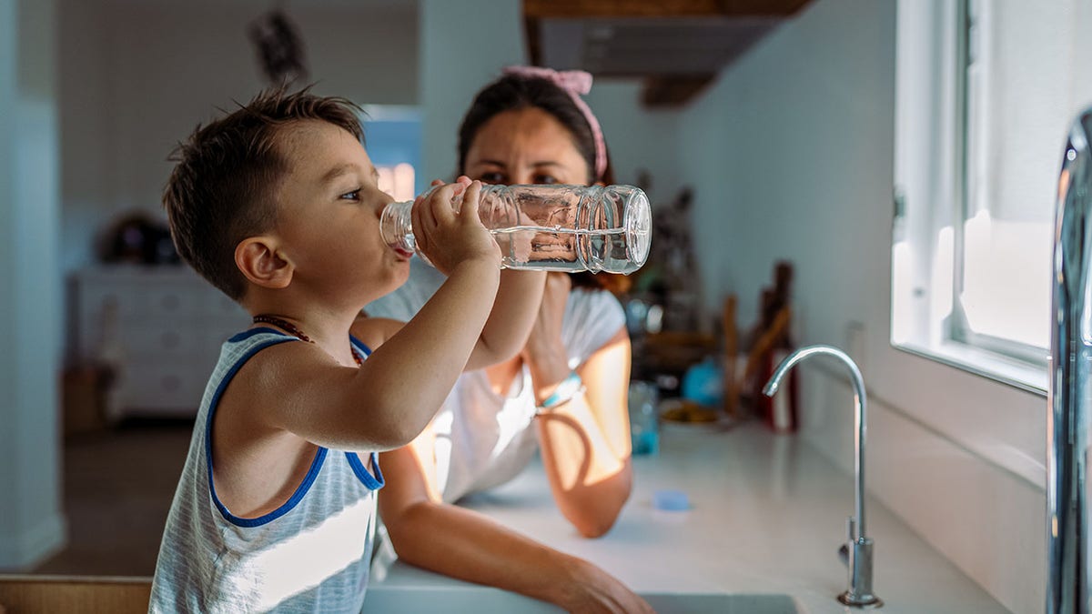 Mother and her toddler drinking a glass with water from the tap