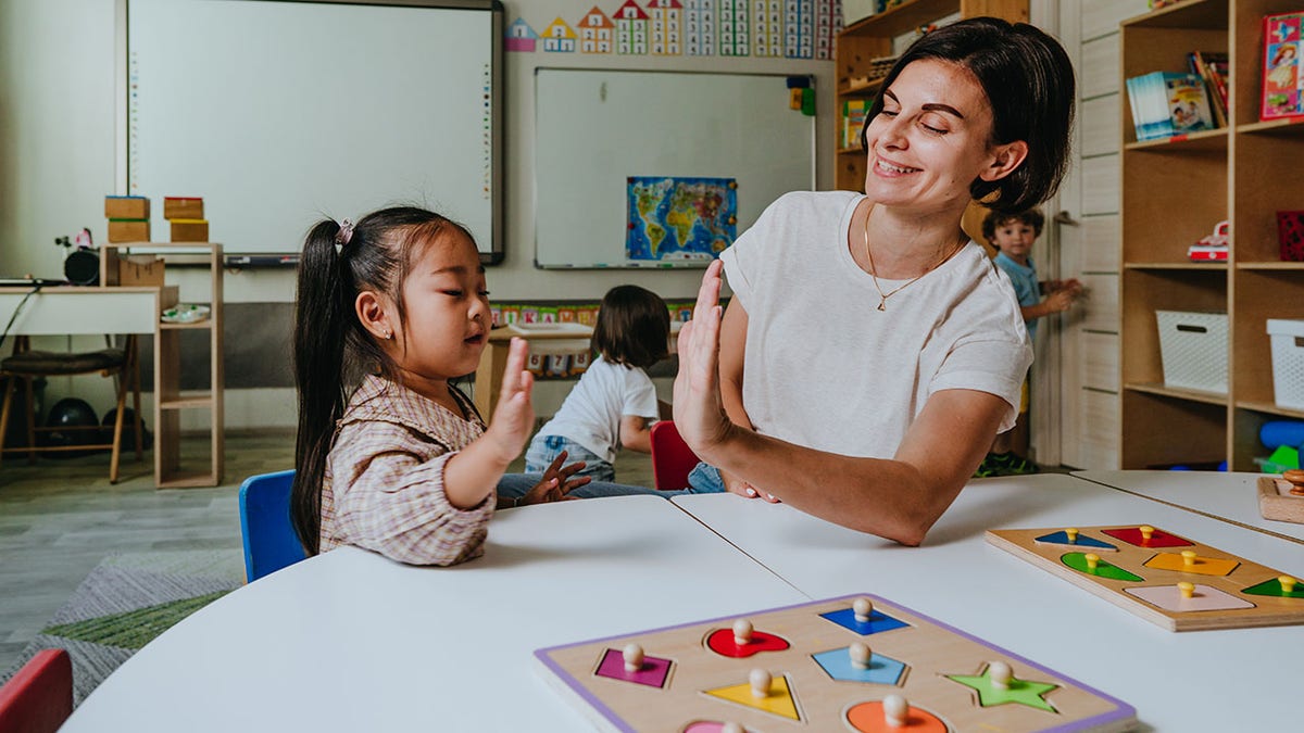 Girl and teacher playing with wooden puzzle in classroom