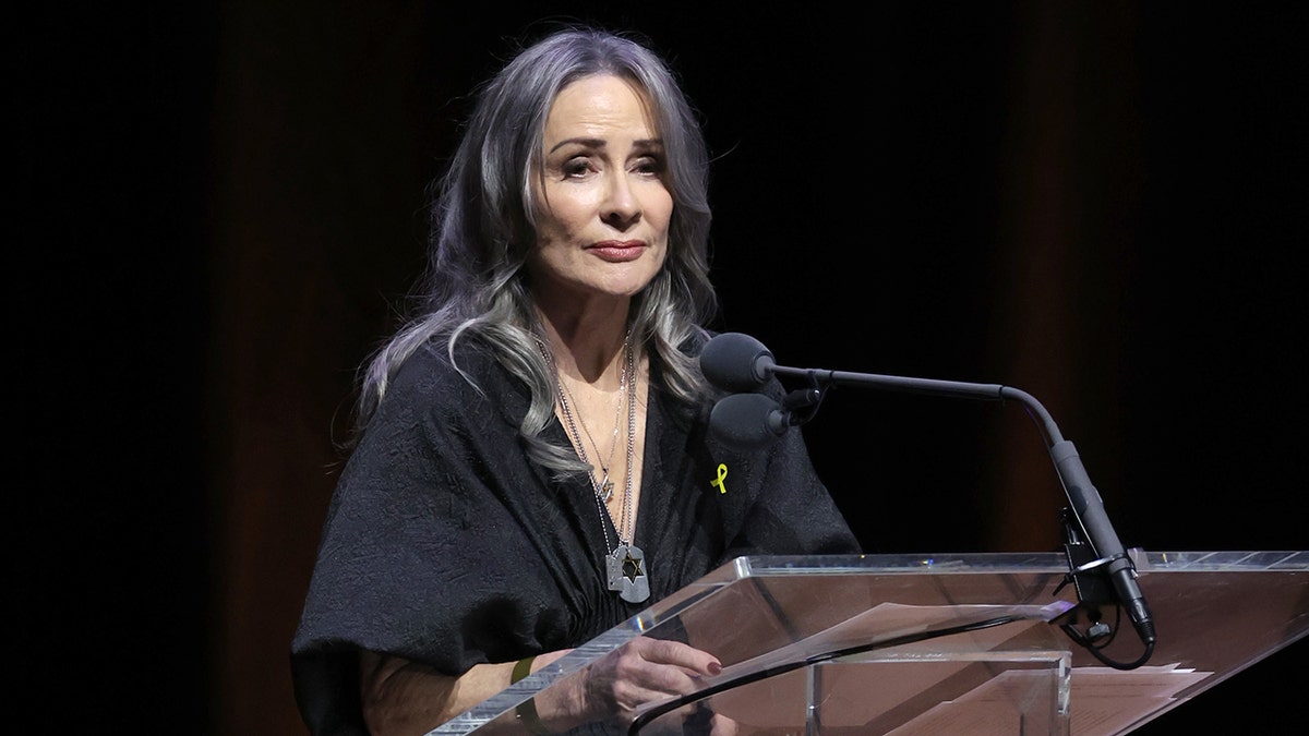 Patricia Heaton stands behind a podium in a black top speaking