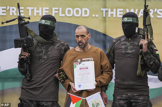 Israeli captive Eli Sharabi stands on a stage escorted by Hamas fighters before being handed over to the Red Cross in Deir al-Balah