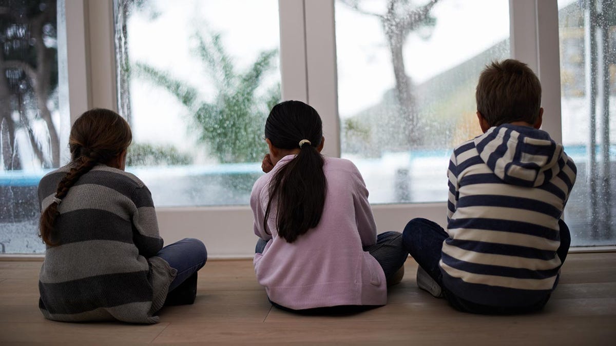 Rearview shot of three children looking out the window on a rainy day