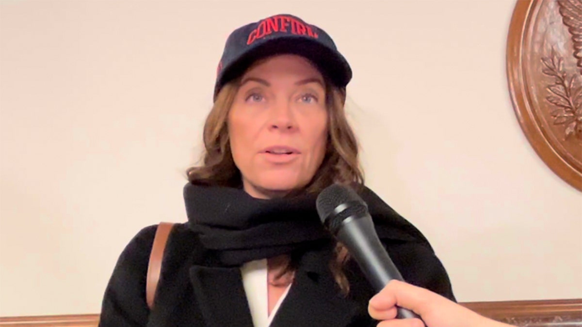 Woman in confirm RFK hat speaking into a microphone.